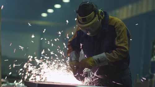 Schwerindustriearbeiter in einer Fabrik arbeitet mit Metall auf einem Winkelschleifer, während heiße Funken pr