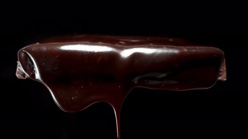 Moving downward following a drop of dark chocolate dripping from a chocolate bar, close-up.