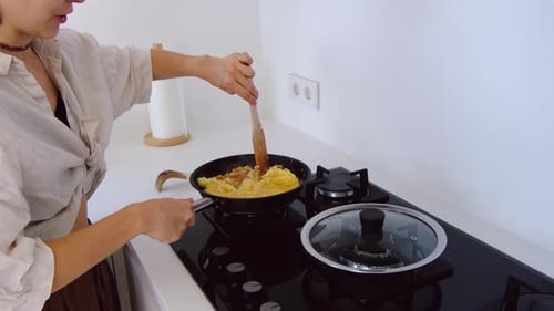 Young Woman Cooking Scrambled Eggs in Modern Kitchen