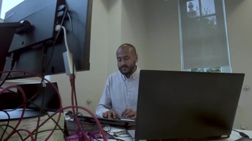 Asian male software engineer sitting at table at company office and working in multiple computers. M