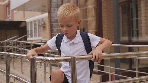 A Schoolboy with a Backpack He is Playing on the Railing After School