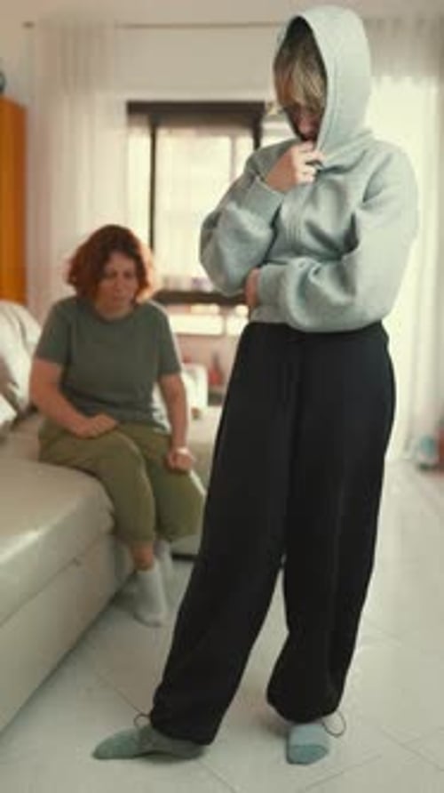 Young Person Stands with Head Down in Sweatpants While Another