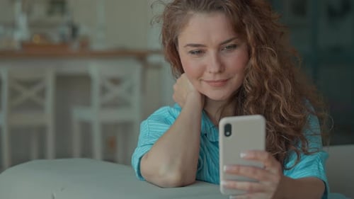 Woman Smiles Using Cellphone Relaxing on Sofa