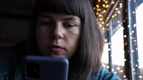 Woman Looks at Smartphone in a Cafe