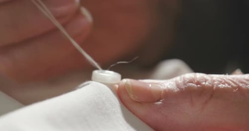 A hand of a young seamstress sewing a white cloth tailoring according to the tradition of tailors.