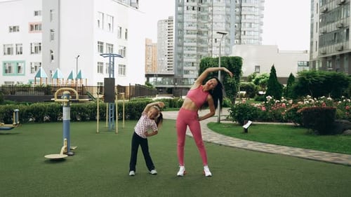 Mother and Daughter Stretching Together in a City Park on a Sunny Day
