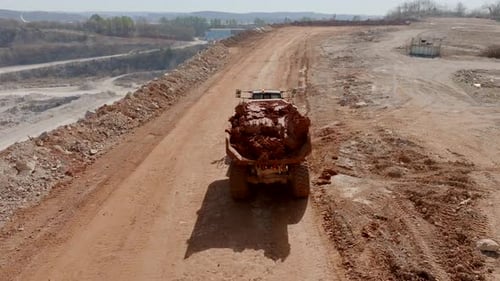 Aerial footage following a construction dump truck full of clay driving up a hill.