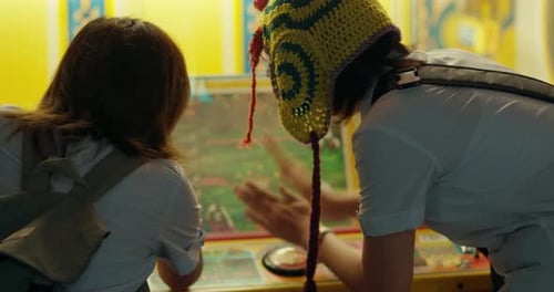 Rearview of girl in knitted headwear hitting button at carnival game with friend