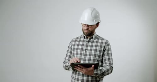 Engineer in Hardhat Reviews Blueprints on Tablet