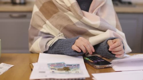 Person Wrapped in Warm Blanket Calculating Money Bills Utilities Checks Kitchen