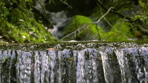 Small Waterfall with Water Flowing in Slow Motion in Creek with Rocks and River in Background