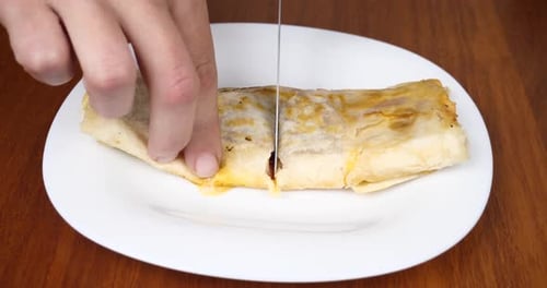 Hand mit Messer Käsebrötchen mit Tomaten und Wurst in Lavash auf einem Teller schneiden