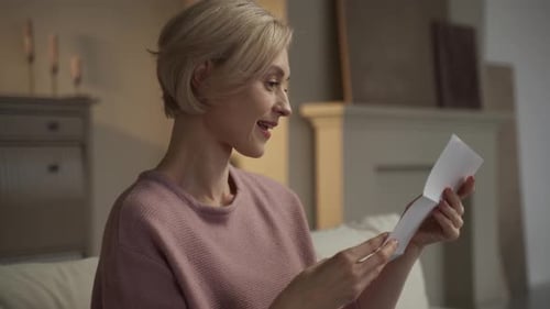 Woman Smiles Reading Letter at Home on Couch