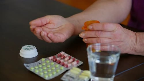 Close Up View of Elderly Hands Pouring Pills From an Orange Prescription Bottle Into the Palm with