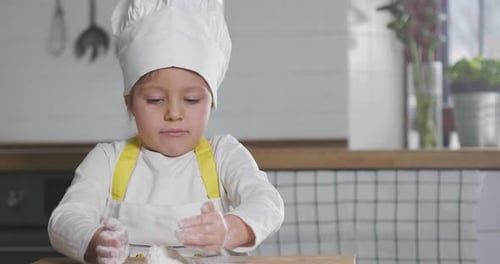 Portrait of a little girl in the kitchen dressed as a professional cook playing with flour, gets h