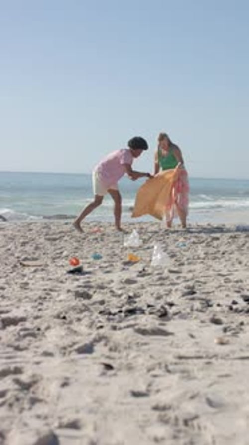Vertical video: Cleaning beach, group of friends picking up trash from sand near ocean