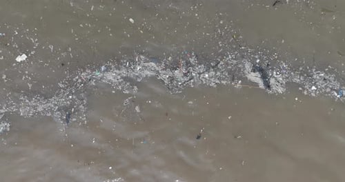 Low altitude ascending top down drone shot of polluted water filled with floating trash and muddy ri