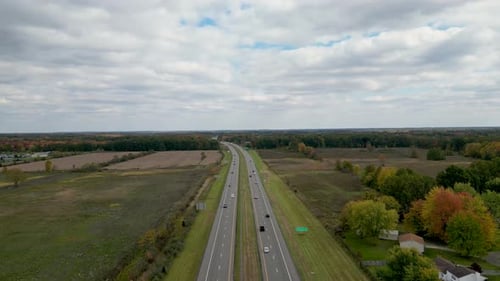 An expansive aerial view of a highway cutting through open fields and a forest under a cloudy sky. I