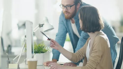 Young Man and Beautiful Woman Discuss Working Issues at Workplace. She Sits at the Table. He Stands