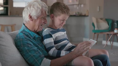 Senior man and child using tablet on sofa