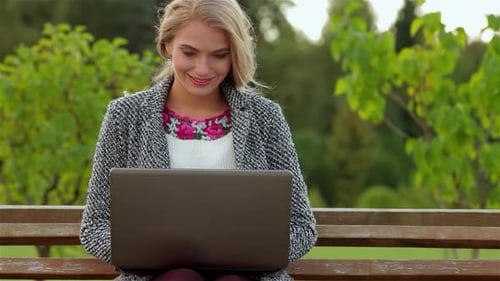 Smiling Girl Student Joyfully Uses a Laptop on a Sunny Park Bench