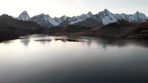 Aerial flyover over a half frozen lake during autumnn sunset with a reflection of the Alps