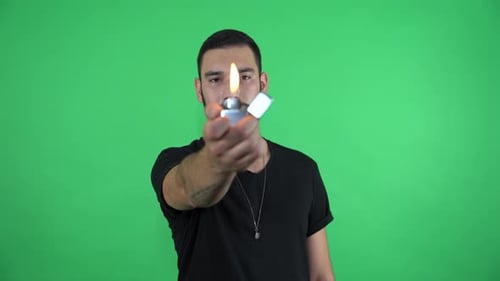 Young man lighting fire with zippo on green screen 4K