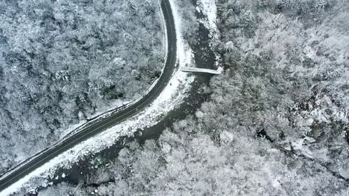 Top Down Aerial View of Snowy Forest Road and River in Winter