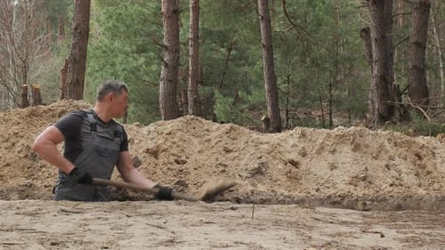 Construction Worker Digging Trench in a Forested Area During Daytime