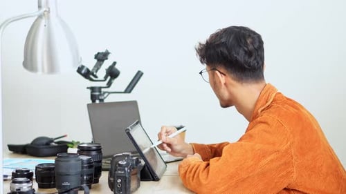 Young Adult Using Tablet at Desk With Camera Equipment