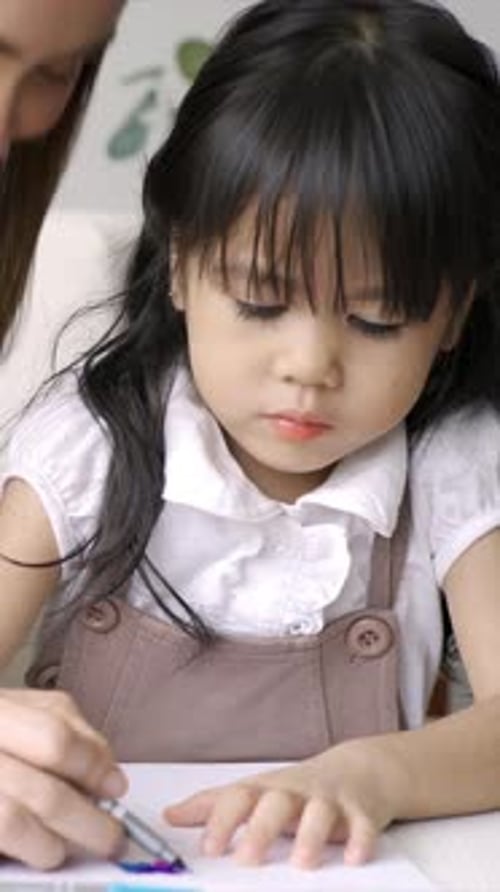 Ein junges, asiatisches Kind arbeitet und spielt zu Hause mit seiner Mutter und lernt in der gemütlichen Umgebung Lesen und Schreiben