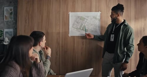 Group of People Review a Map While Discussing Plans They Use Laptops and Take Notes