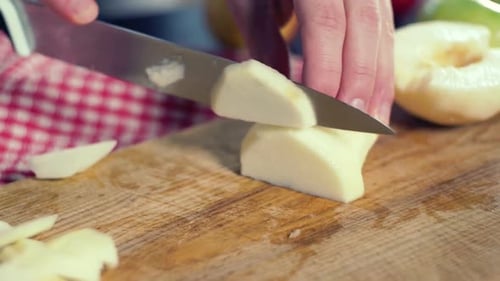 Der Koch schneidet frische reife Apfelscheiben auf einem Holzbrett in der sonnigen Küche