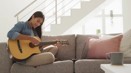 Woman Plays Guitar on Couch at Home