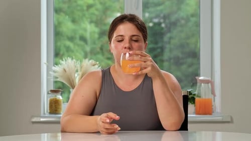 Woman Drinks Orange Juice at Kitchen Table