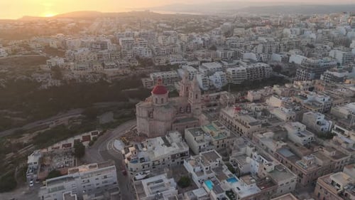 An aerial view of the Mellieha Parish Church with its red dome and twin towers. The surrounding