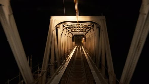 Eisenbahnschienen und fahrender Zug auf einer Brücke in der Nähe von Strommasten in dunkler Nacht