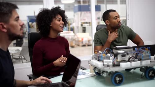 Multiracial team of engineers collaborating on a robotics project in a modern factory, discussing st