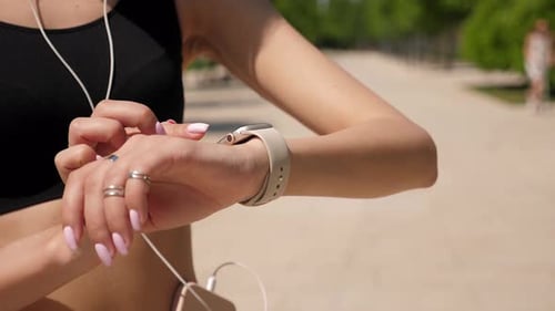 A Sporty Woman Checks the Data on Her Smartwatch After Jogging in the Park