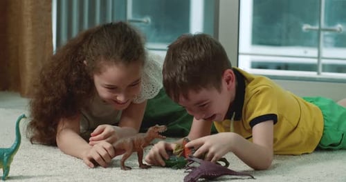 Two Happy Children Kids Play with Dinosaurs on the Floor While Lying on the Carpet at Home Concept