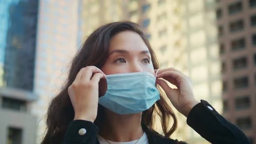Woman Putting on a Medical Mask in City