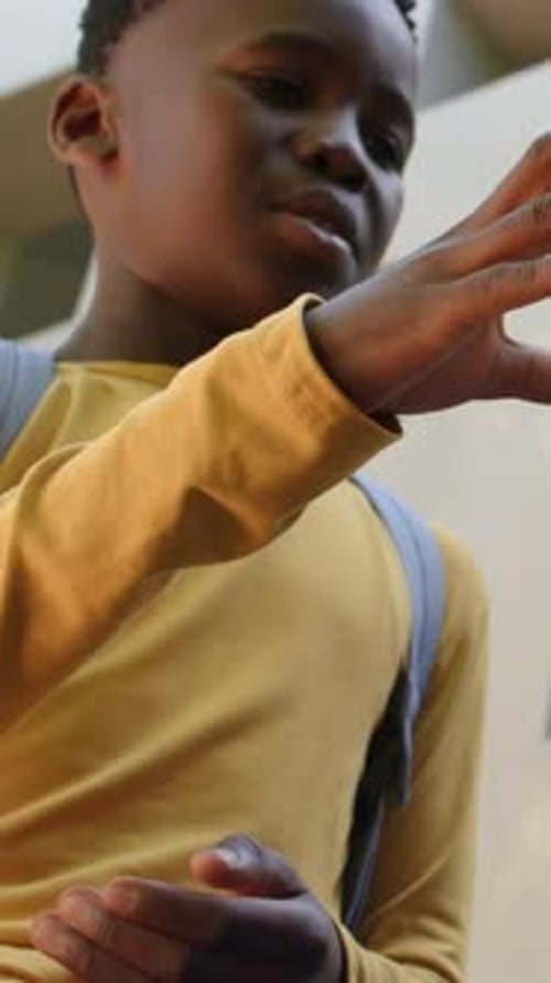 Vertical video: Rubbing boy in yellow tee with bag at wall showing hand motions mirroring denim arm