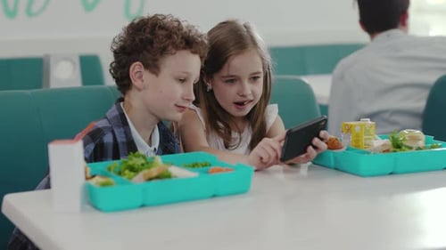 Los niños disfrutan felizmente del almuerzo mientras interactúan juntos con la tecnología y entre ellos