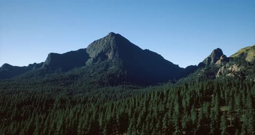 Majestic Mountain Peak Rises Above Lush Green Forest Under Clear Sky