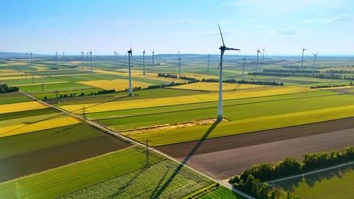 Blades of multiple windmills rotate slowly in the wind. Green energy production in the wind farms.
