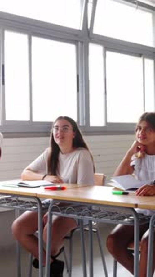 Happy Group Diverse Elementary School Students Sitting in Classroom Attending By Raising Their Hands