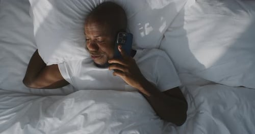 Un gars endormi à peine éveillé répond et parle sur un smartphone alors qu'il est encore allongé dans son lit