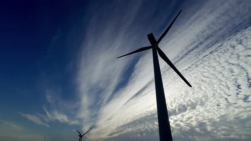 Close shot of a windmill in contrast to the sunny blue sky with clouds, its fins move slowly, countr
