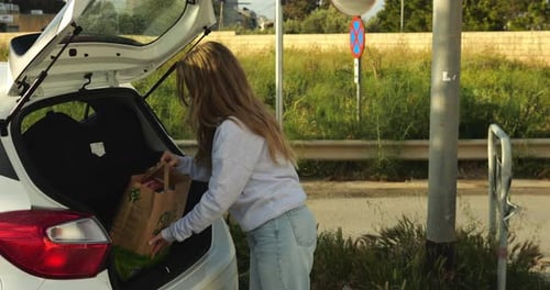 Mujer joven carga una bolsa de papel reciclable ecológica con sus compras en el maletero del automóvil