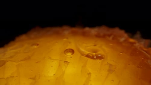 Honey being poured onto golden honeycombs against a black background. Macro Dolly